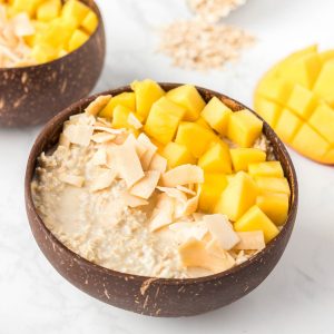 Mango overnight oats in a wooden bowl with mango chucks and coconuts flake on top.