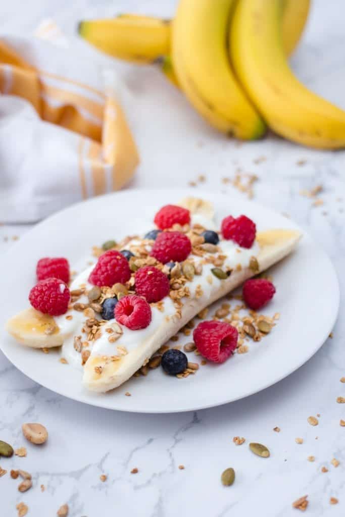 Breakfast Banana split on a white plate with banana in the background