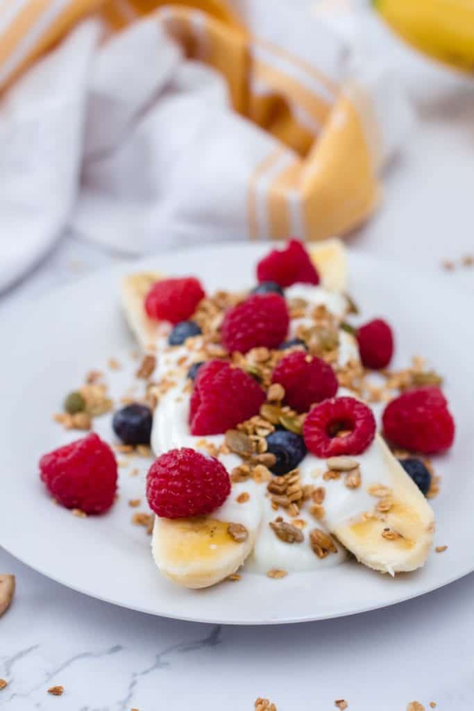banana with berries, granola and yogurt on a white plate 
