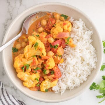 Cauliflower Chickpea Curry serves in a bowl with a spoon tp view.