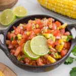 corn pico de gallo in a serving bowl with slice of lime on too.