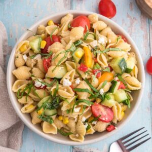 Pasta salad in a serving bowl with cherry tomatoes on the side.