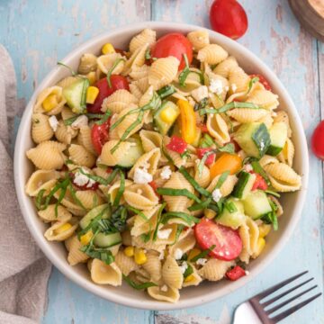 Pasta salad in a serving bowl with cherry tomatoes on the side.