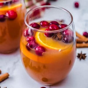Apple cider serve in a glass with cranberries and oranges slices as a garnish