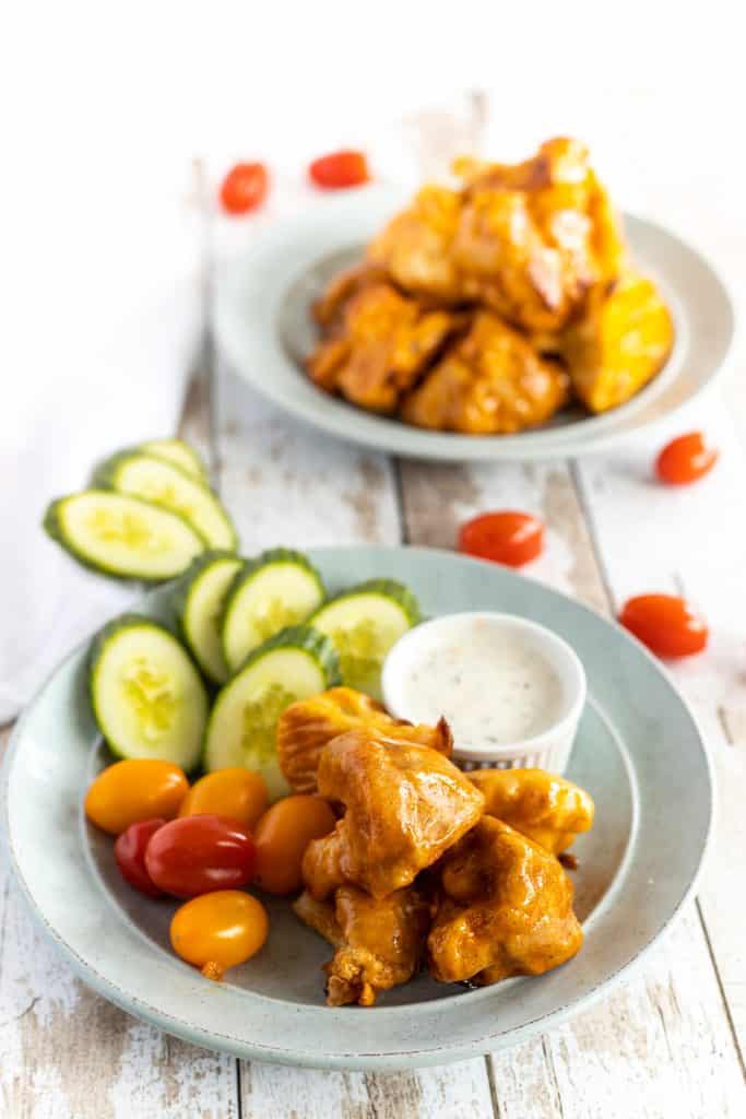 cauliflower wings in plate with sliced cucumber and cherry tomatoes