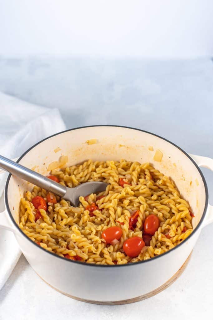 preparing the  dish, the pasta in a pot with the broth and cherry tomatoes 