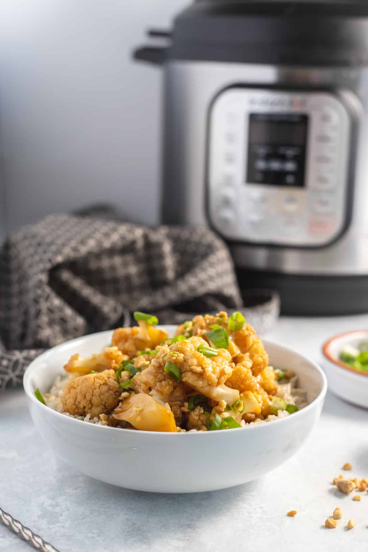Vegan kung Pao Cauliflower in the Instant Pot in a bowl on top of rice with instant pot in the background
