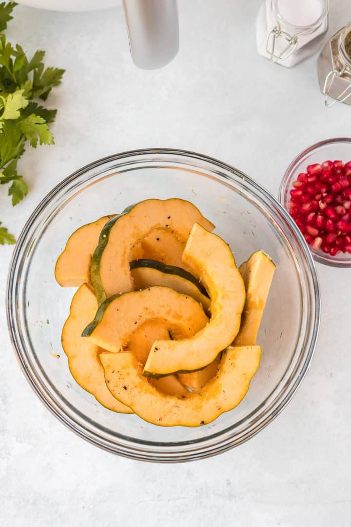Slice acorn squash in a bowl with olive oil