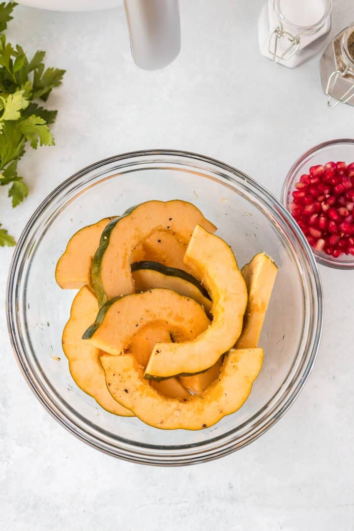 Slice acorn squash in a bowl with olive oil