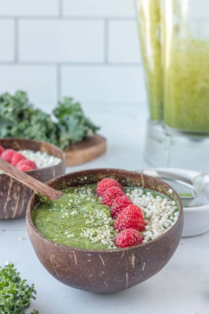 Matcha smoothie serve in a coconut bowl with raspberries on top and a spoon 
