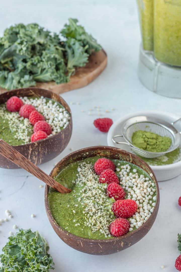 Matcha smoothie bowl serve in a coconut bowl with raspberries and puffed quinoa on top