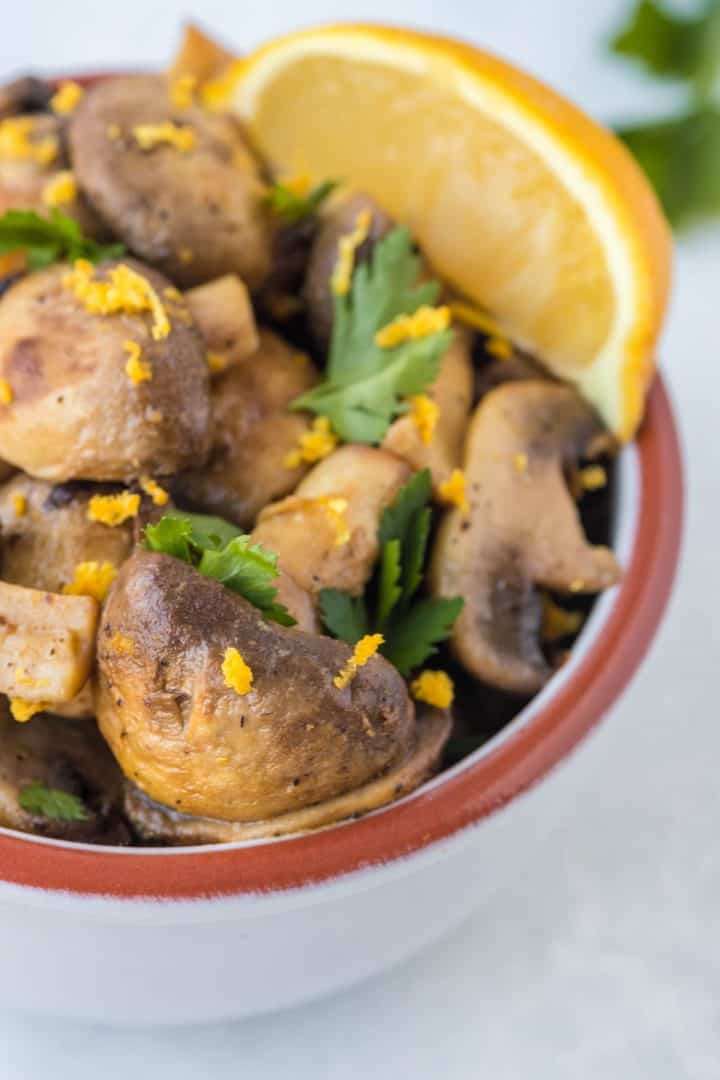 Close up of the Air Fryer Garlic and Lemon Mushroom cooked  in  small bowl with lemon zest and parsley on top .