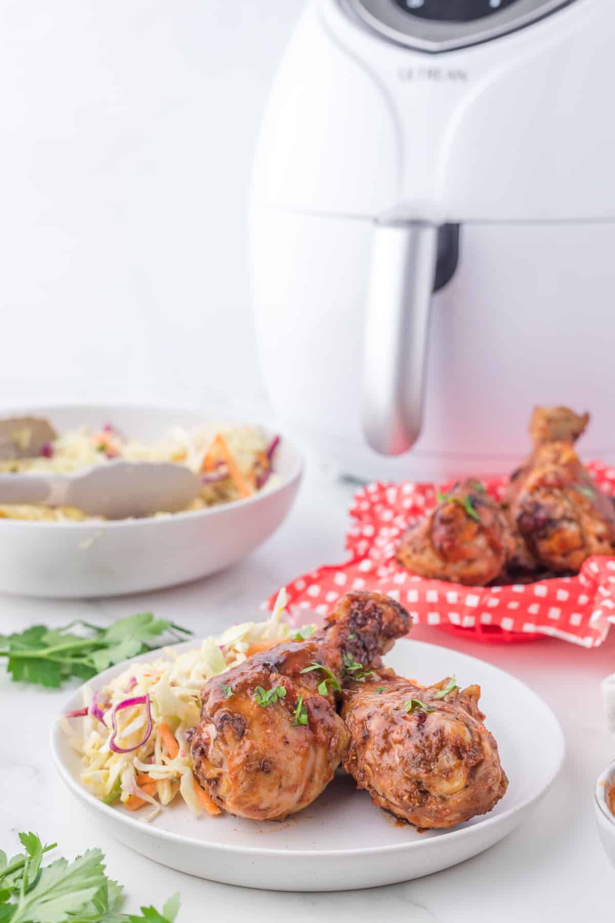  Air Fryer BBQ chicken drumsticks, in a white plate with Air fryer in a background.