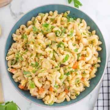A bowl of 4 ingredients Macaroni Salad with chopped vegetables and fresh herbs, served in a blue bowl on a marble surface.