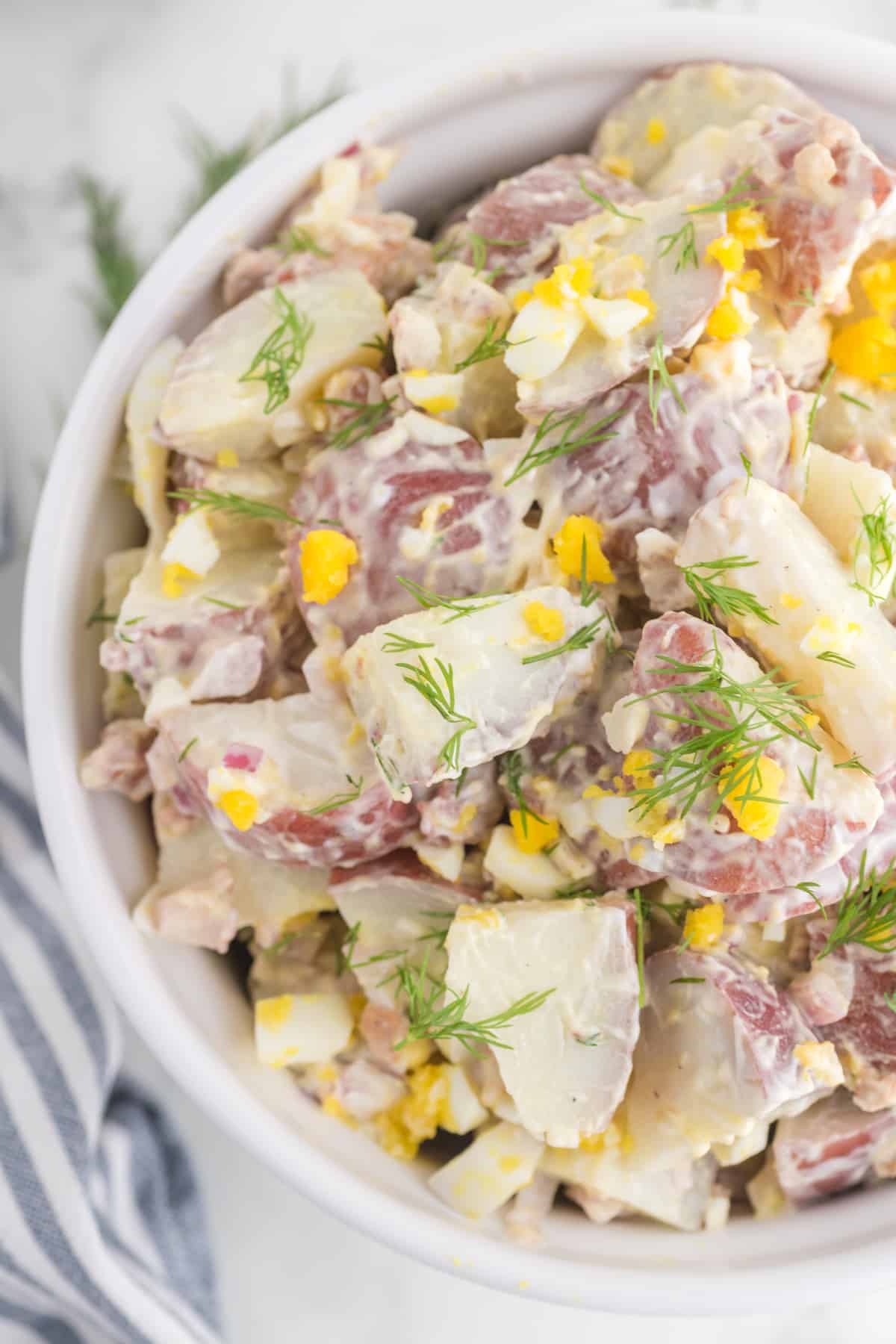 potato salad serve in a white bowl close up.