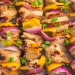 Easy teriyaki chicken skewers on a white plate with sesame seeds and green onions