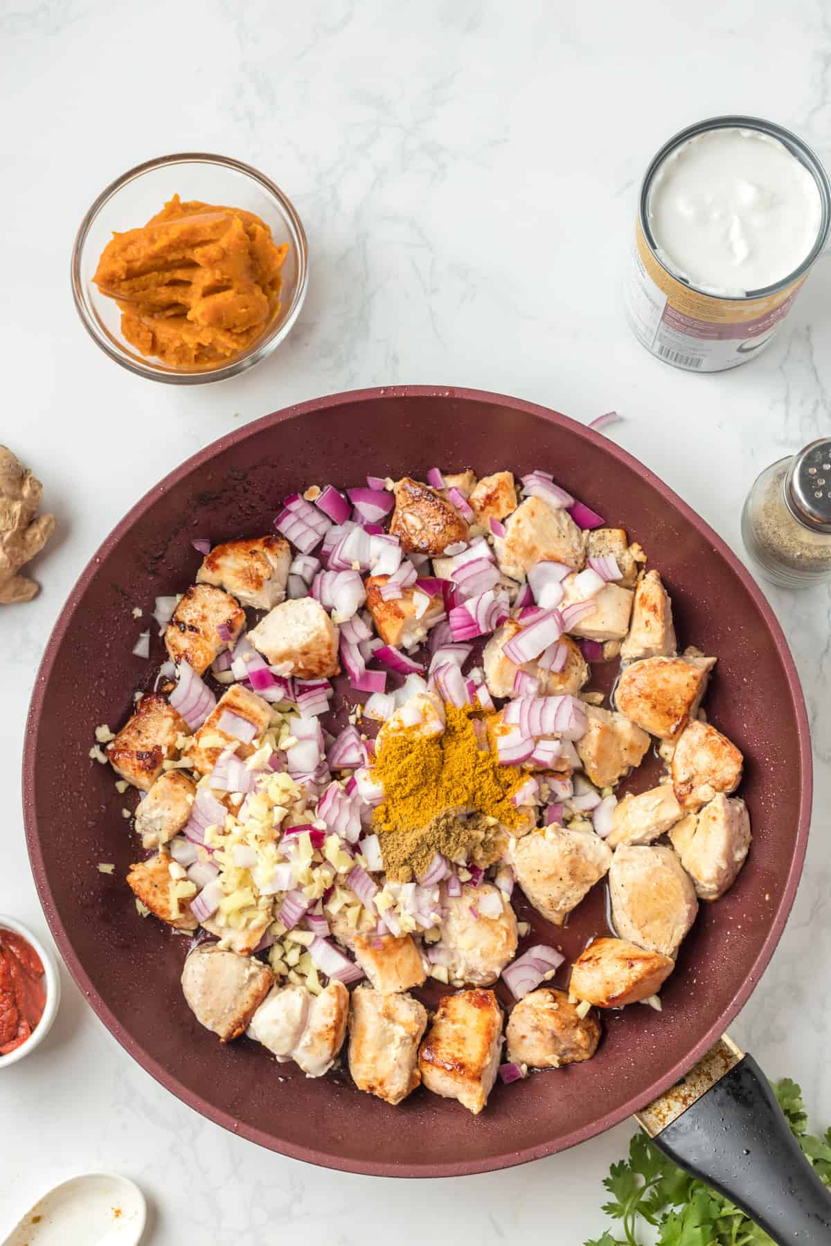 Chicken pieces in the skillet with onion, ginger and spices.