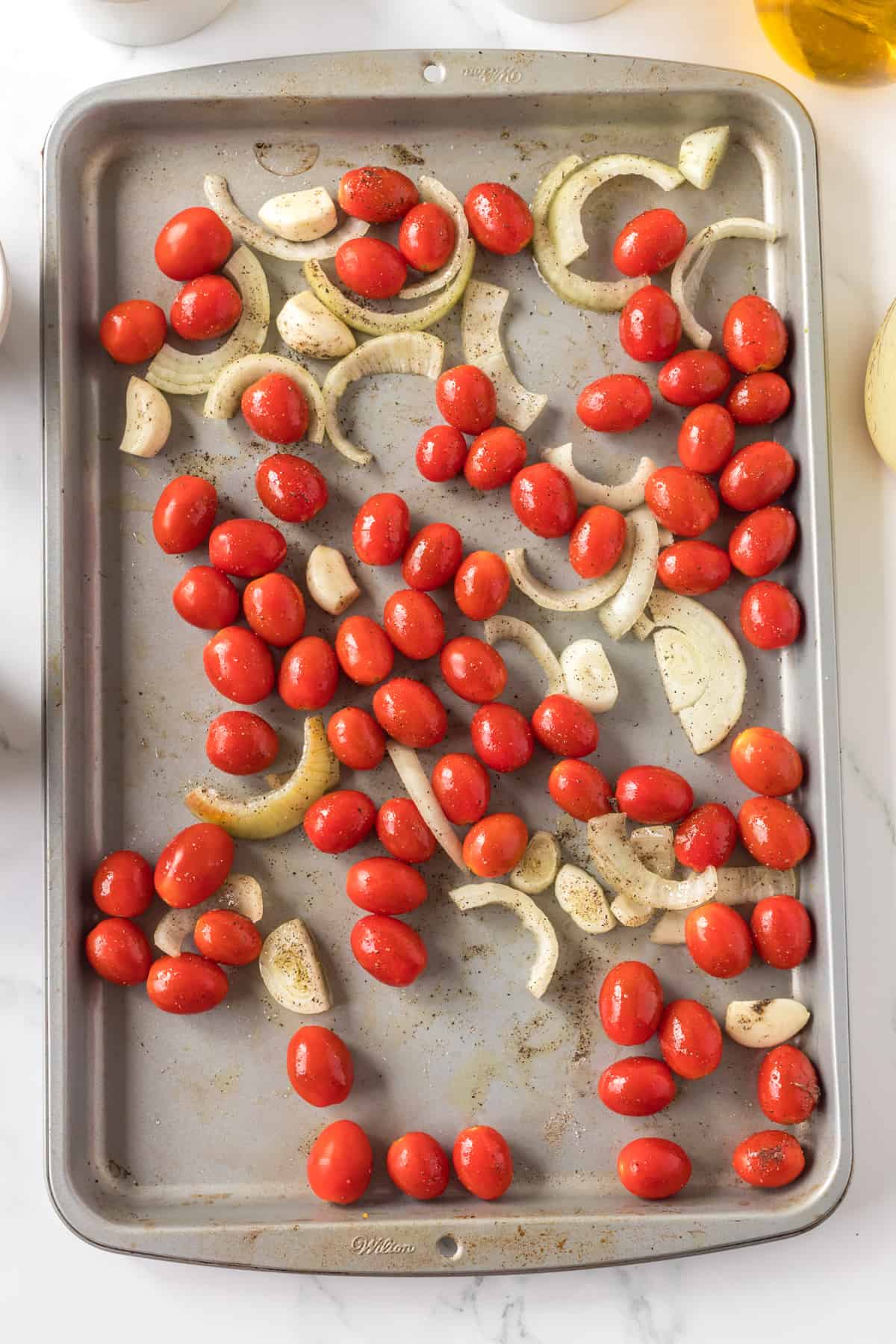 Cherry tomato, onion and garlic on the baking sheet.