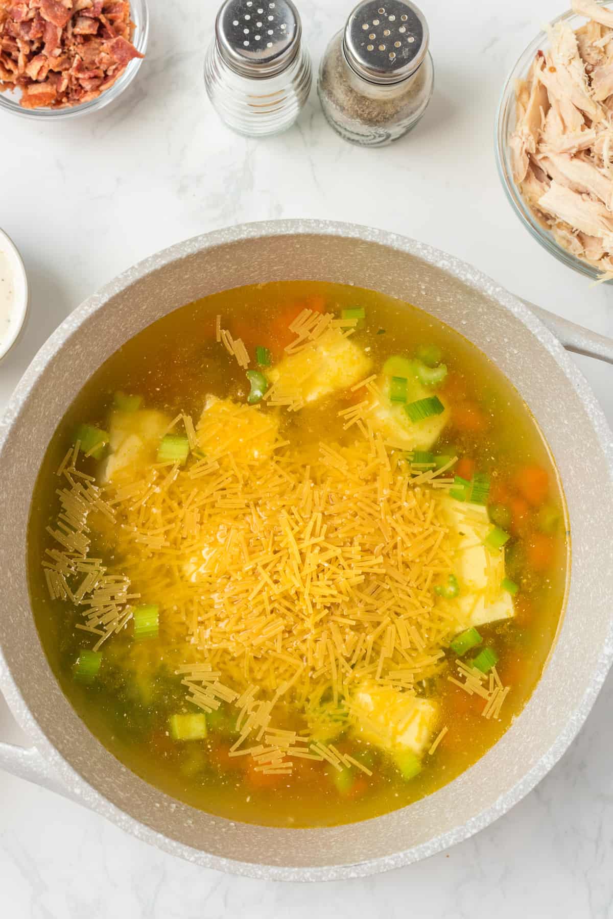 Adding the chicken broth, cream cheese and noodle to the pot.