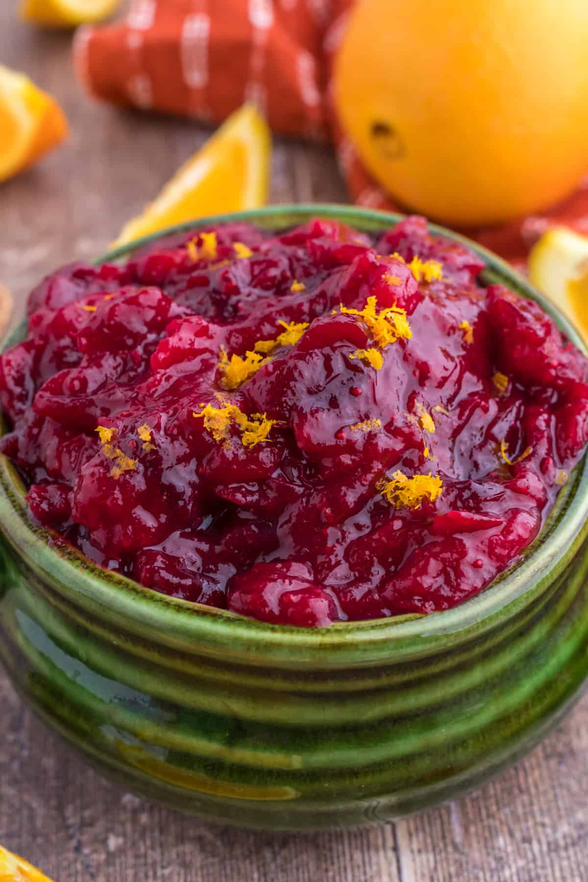 A vibrant green bowl cradles a delectable cranberry orange chipotle sauce, set against a backdrop of zesty orange.