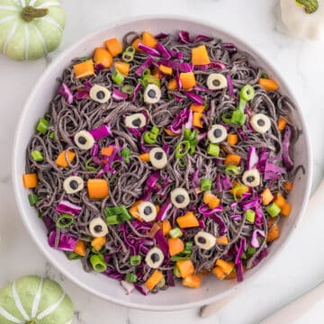 Salad serving in a white bowl with pumpkin and skeletons on the side.