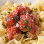 Chicken meatballs serve in a bowl over pasta with tomato sauce.