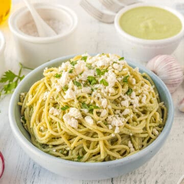 green spaghetti in a bowl with crumble cheese and fresh herbs on top.
