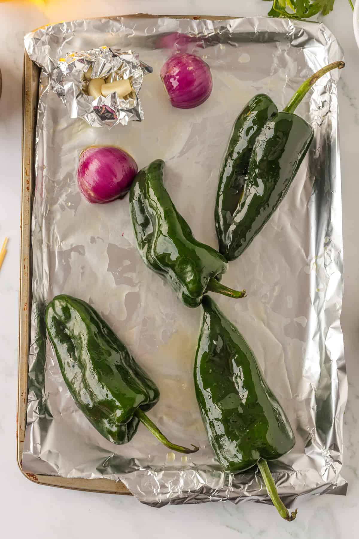 poblano peppers, onion and garlic on a sheet pan ready to be cooked.