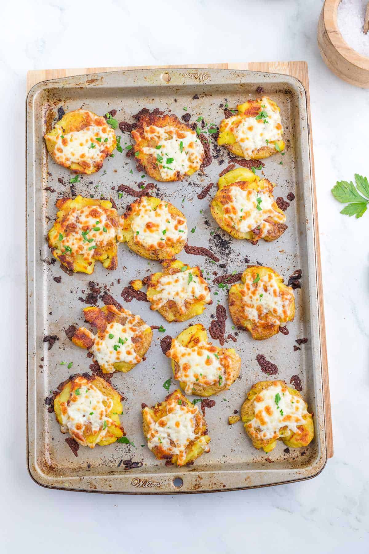 Smashed potatoes on cooking sheets with melted cheese on top.