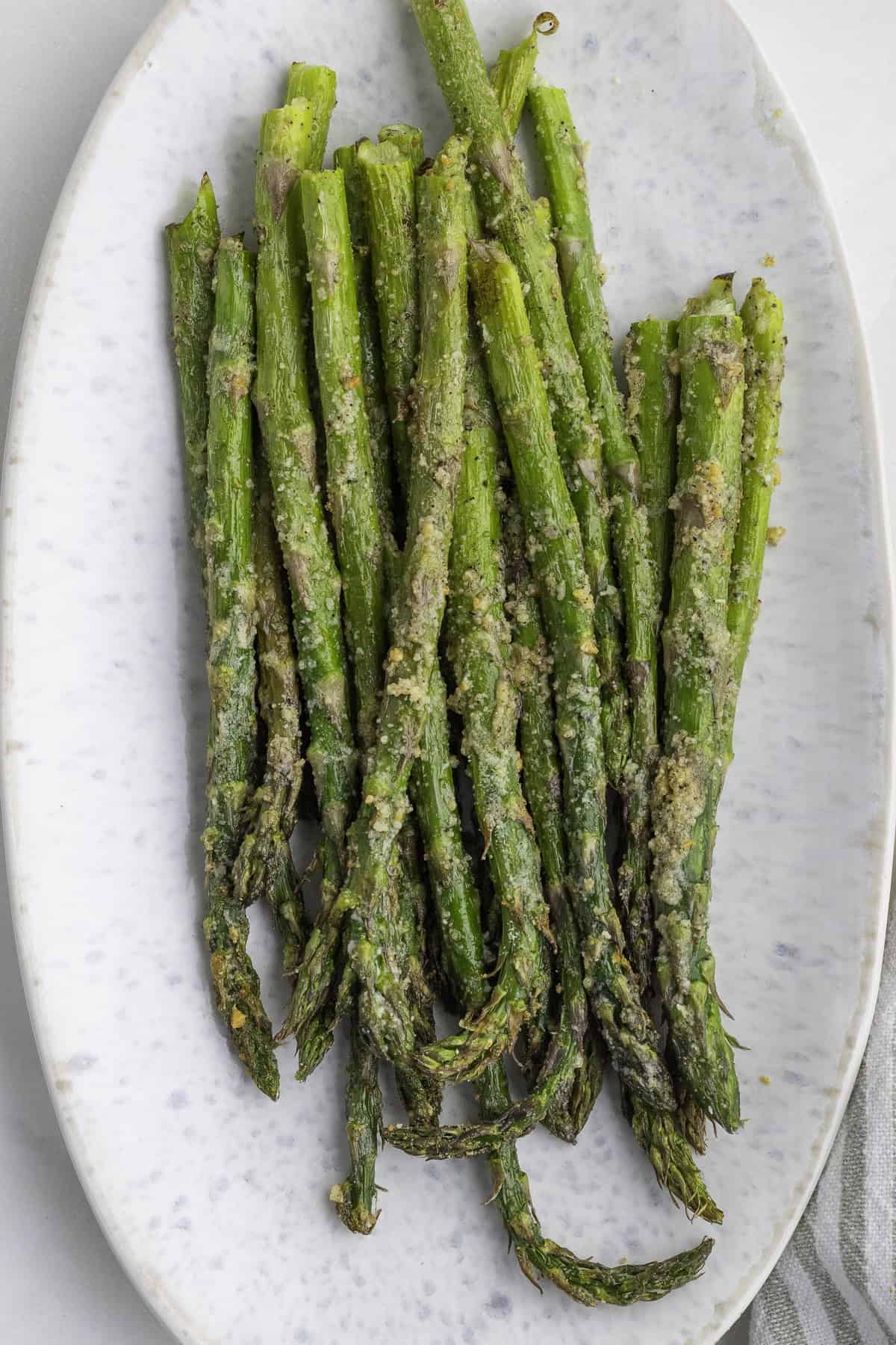 A white oval plate with a serving of roasted asparagus topped with grated parmesan cheese.
