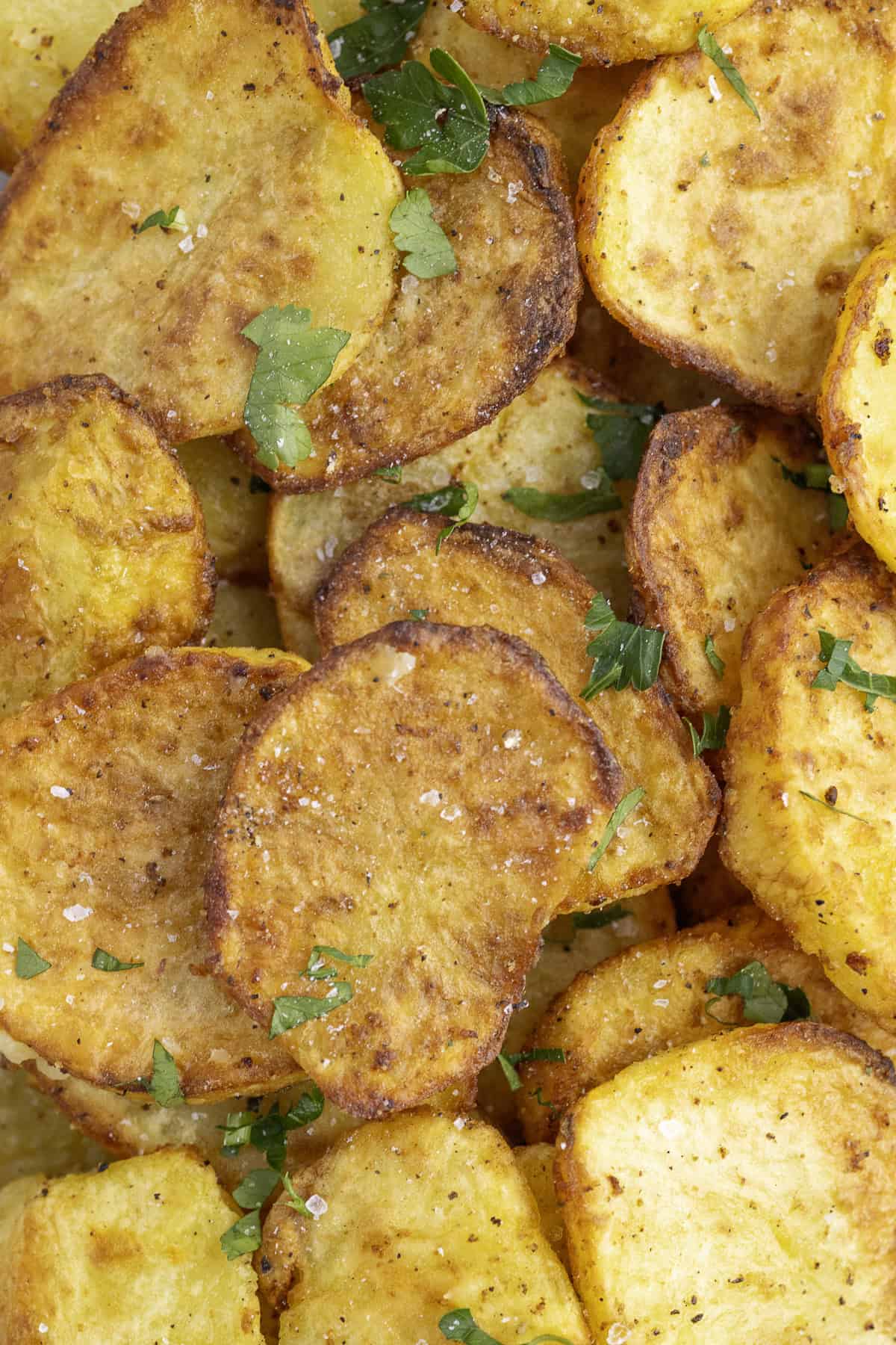 Golden brown roasted potato slices sprinkled with herbs and salt.