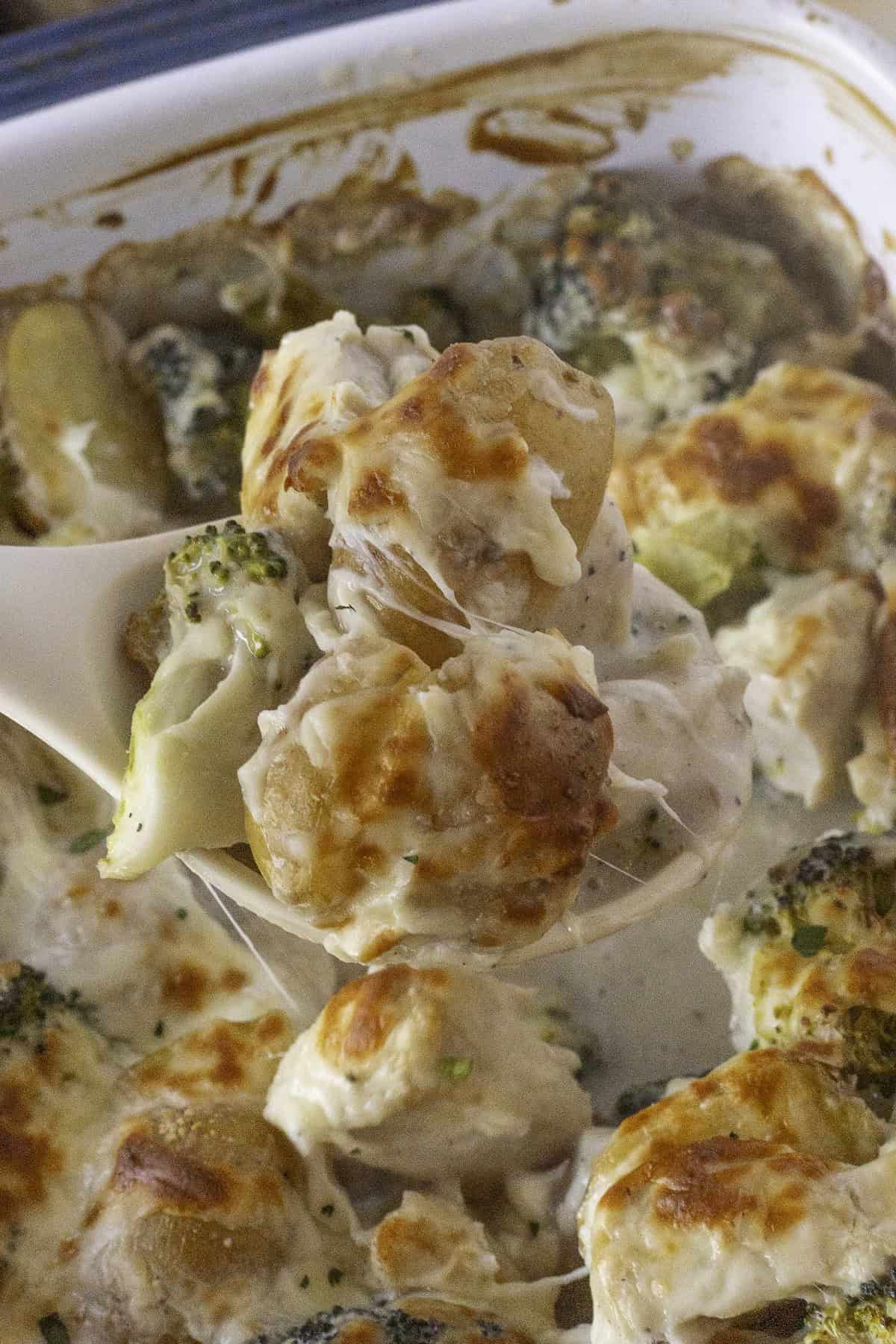 A spoon serving a creamy broccoli and chicken casserole with melted cheese from a white dish.