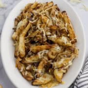 A plate of seasoned fries topped with melted cheese and caramelized onions, served on a white dish.