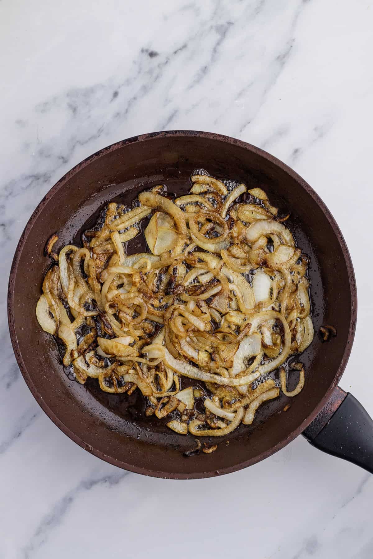 Sliced onions frying in a pan on a marble surface.
