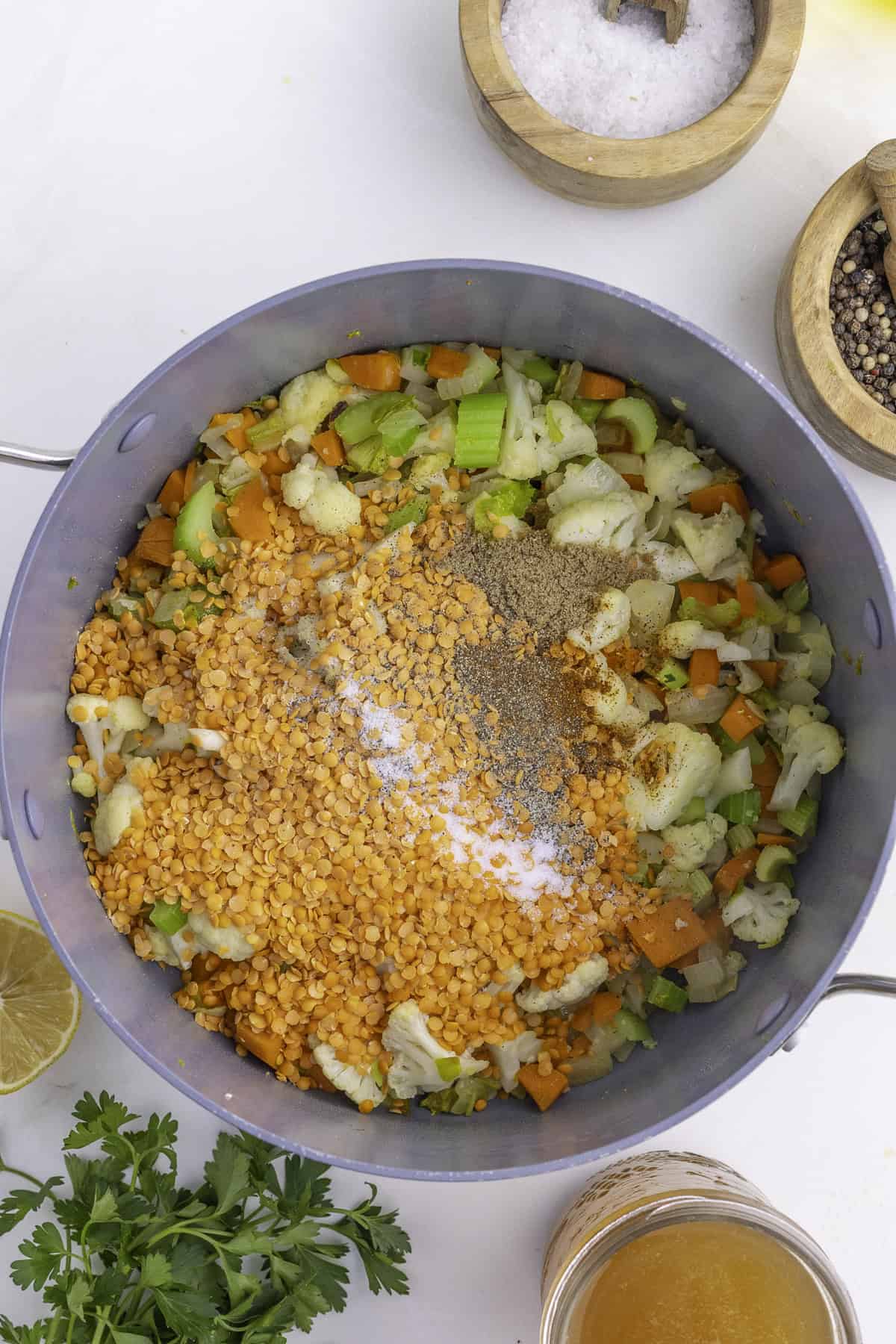 Marmite avec légumes hachés, lentilles et épices. Sel et poivre dans des bols, quartier de citron, persil et bouillon à proximité sur une surface blanche.