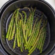 Asparagus spears coated with seasoning are arranged in an air fryer basket.