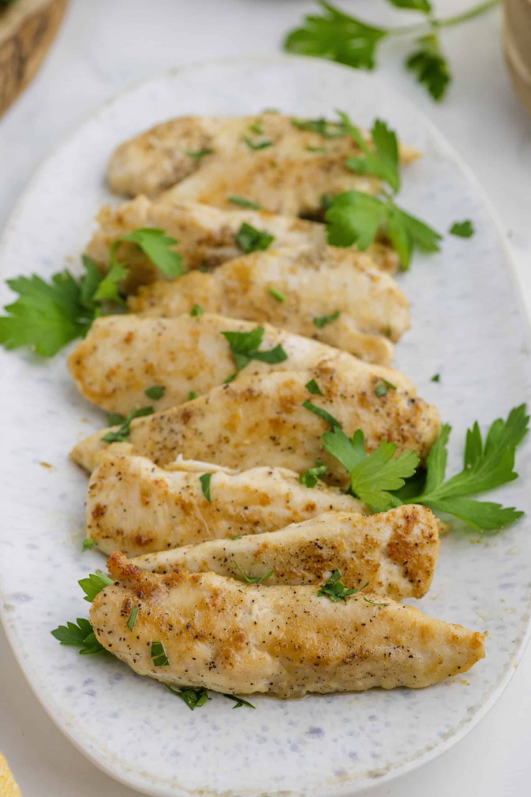 Cooked chicken breast slices garnished with herbs, arranged on an oval white plate.