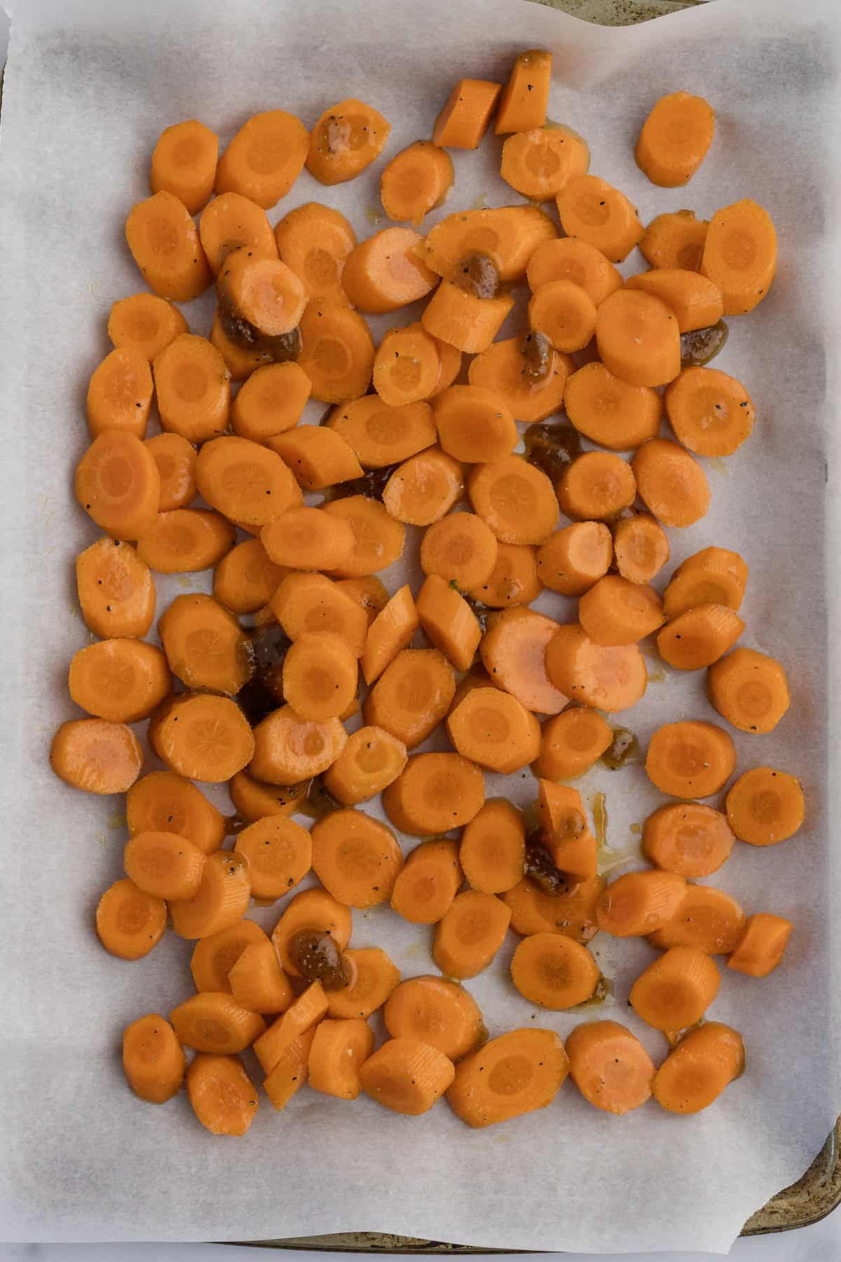 Sliced carrots seasoned and spread on a parchment-lined baking sheet.