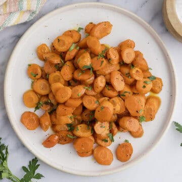A plate of sliced, roasted carrots garnished with chopped parsley on a marble countertop.