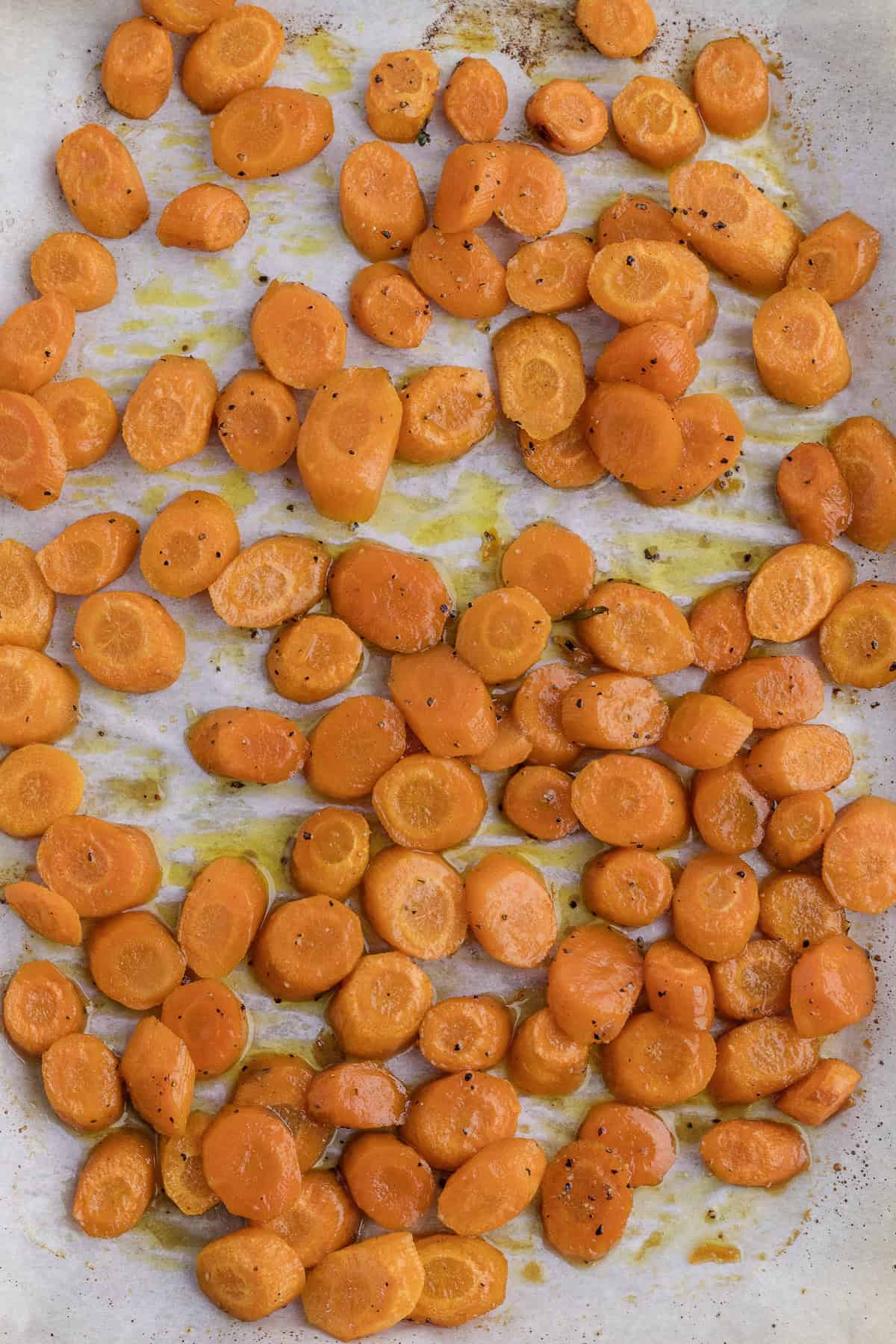 Sliced roasted carrots seasoned with black pepper on parchment paper.