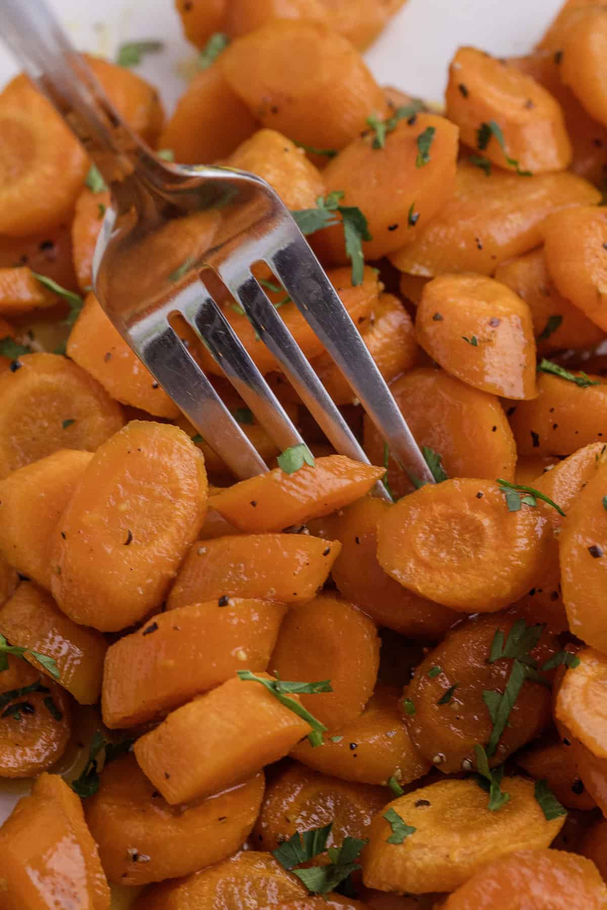 A fork rests on a pile of sliced, cooked carrots garnished with chopped herbs.