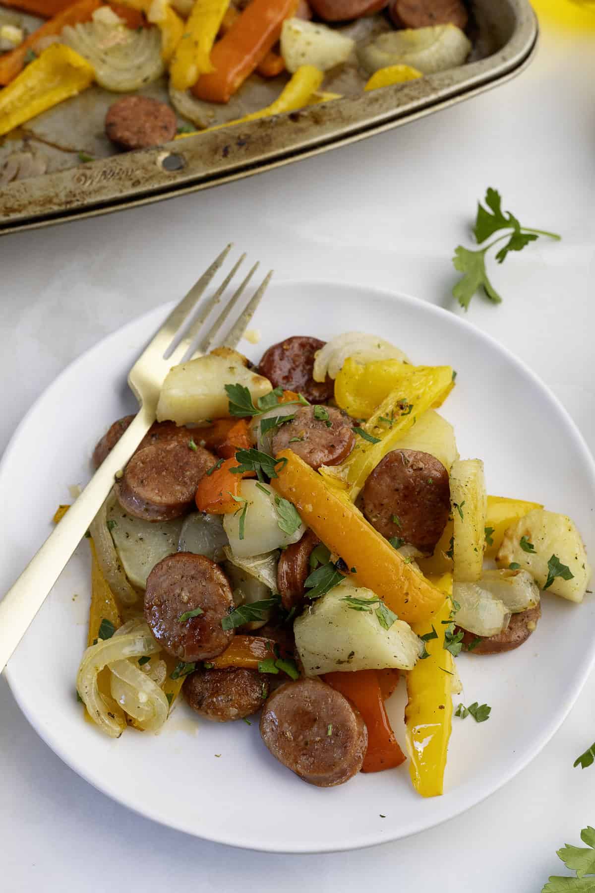 A plate of sliced sausage, yellow and orange bell peppers, and onions garnished with parsley, with a fork resting on the side.