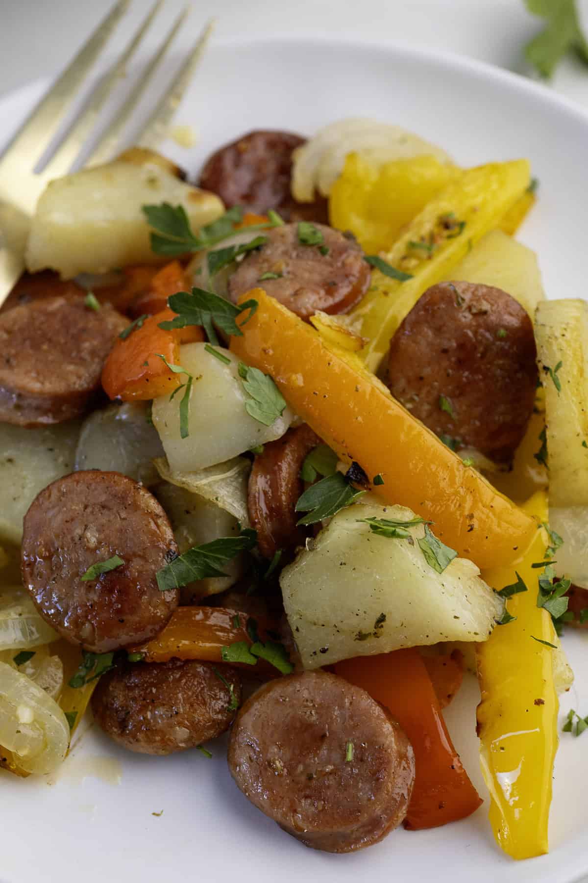 A plate with sliced sausage, yellow and red bell peppers, potatoes, and parsley garnish. A fork is partially visible on the plate.