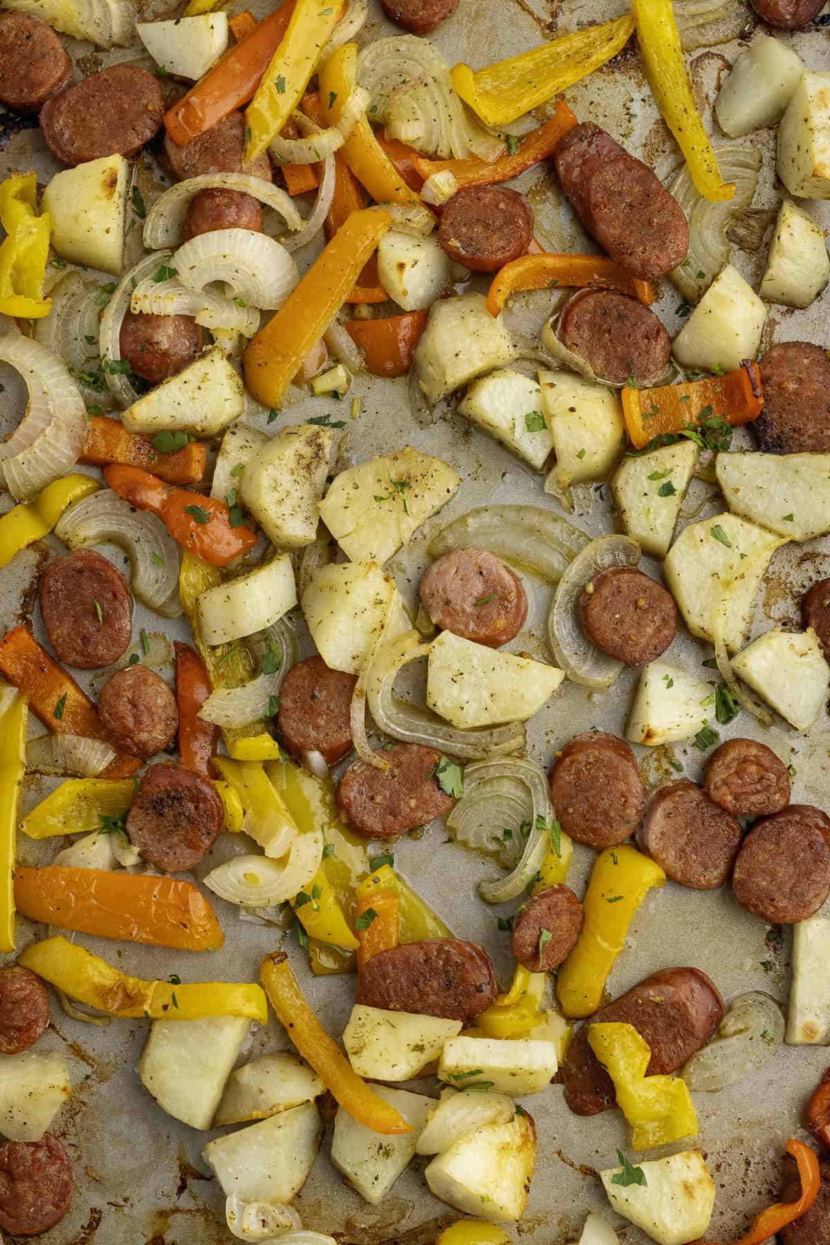 Sheet pan with sliced sausage, potatoes, onions, and bell peppers. Seasoned with herbs and spices, the dish is baked and appears golden brown.