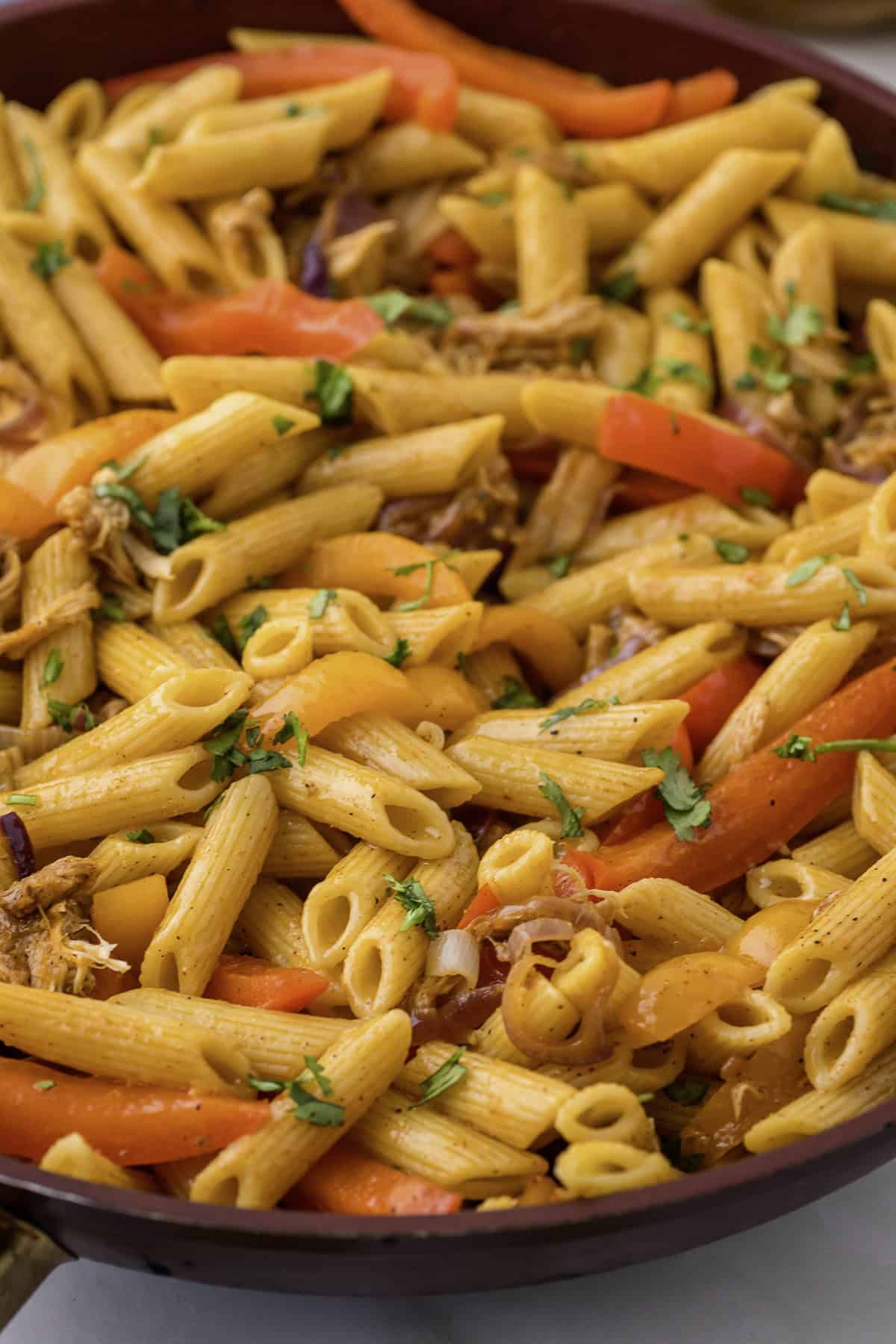 A pan filled with penne pasta, sliced red and yellow bell peppers, and garnished with chopped herbs.