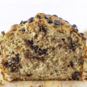 Close-up of a sliced loaf of bread with visible chocolate chips and a moist, textured interior on a wooden surface.