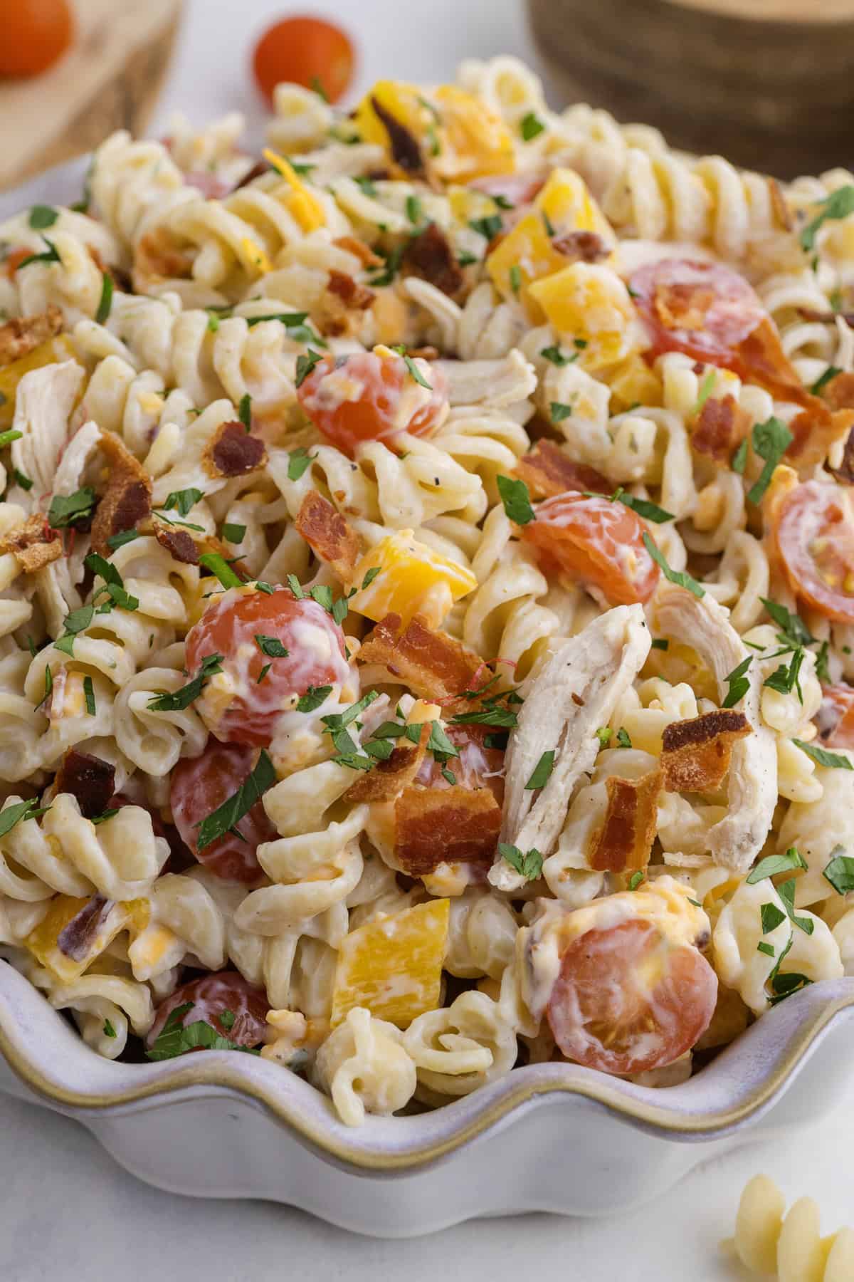 A bowl of rotini pasta salad with cherry tomatoes, shredded chicken, bacon pieces, cheese, and chopped herbs in a creamy dressing.