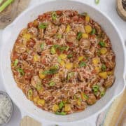 A skillet containing a colorful mix of rice, sausage, yellow bell peppers, tomatoes, and green onions.