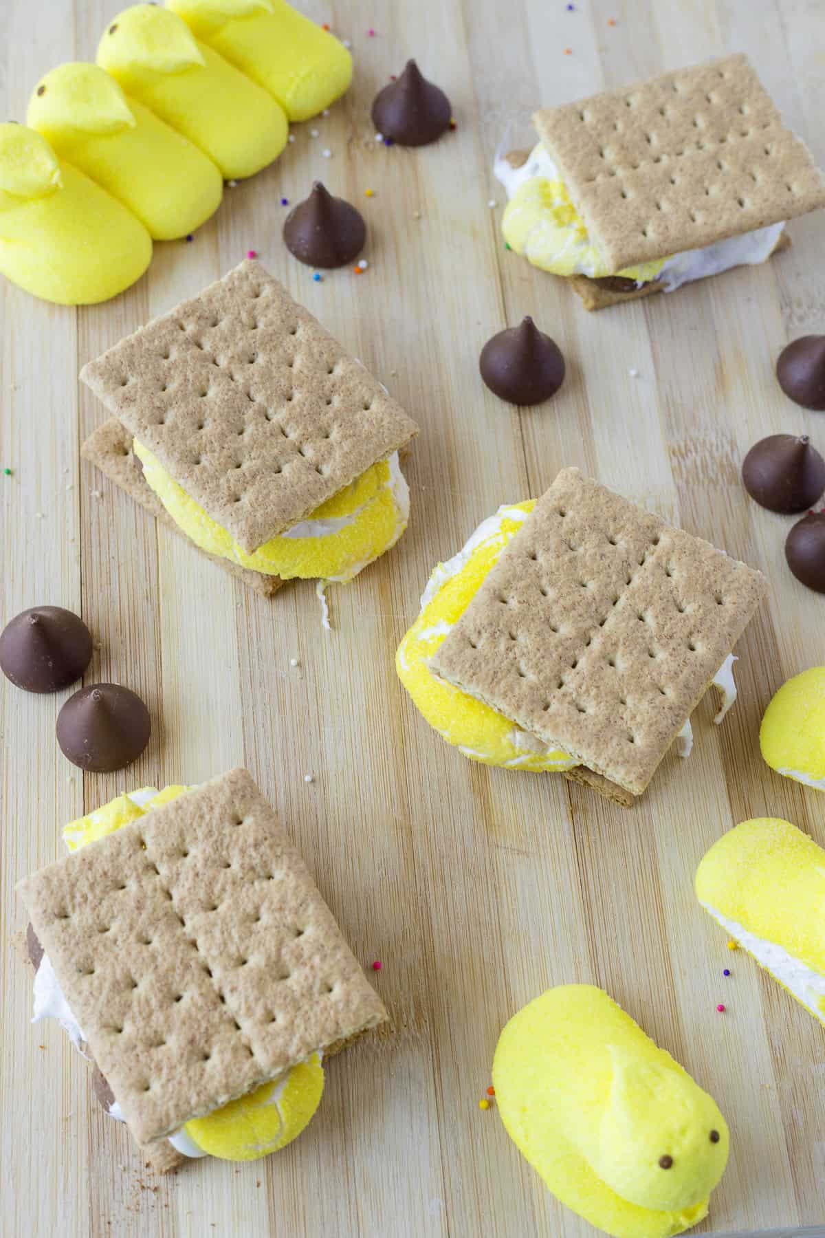 Graham crackers with yellow marshmallow chicks and chocolate pieces on a wooden surface.