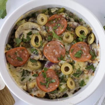 A baked dish in a white bowl featuring sliced mushrooms, pepperoni, olives, green peppers, and melted cheese, garnished with parsley.